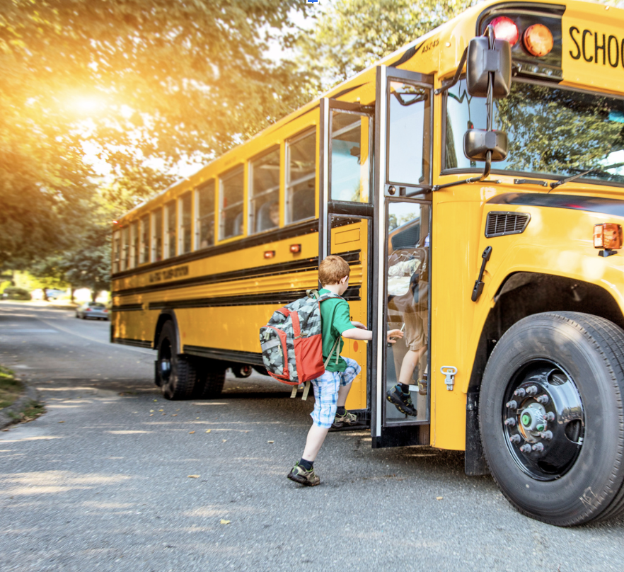 A kid is getting onto a school bus on a sunny day.